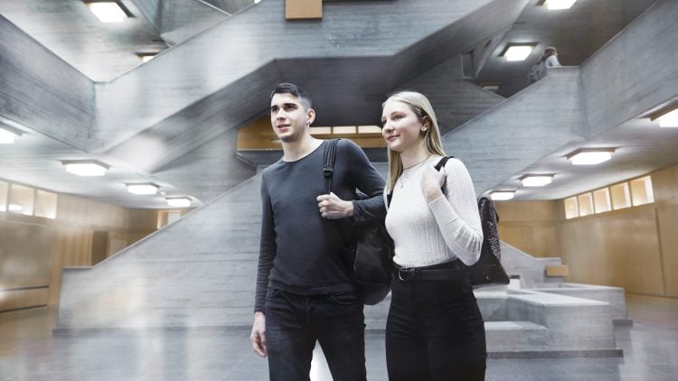 Two smiling young people with backpacks inside IWC building
