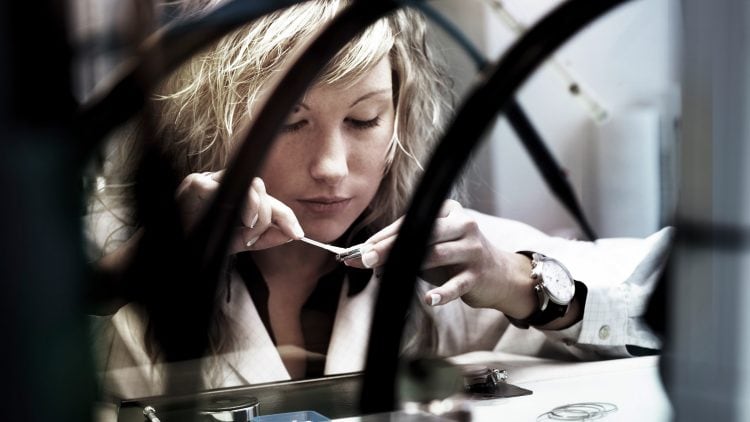 Young woman in white uniform assembling an IWC watch in manufacture environment