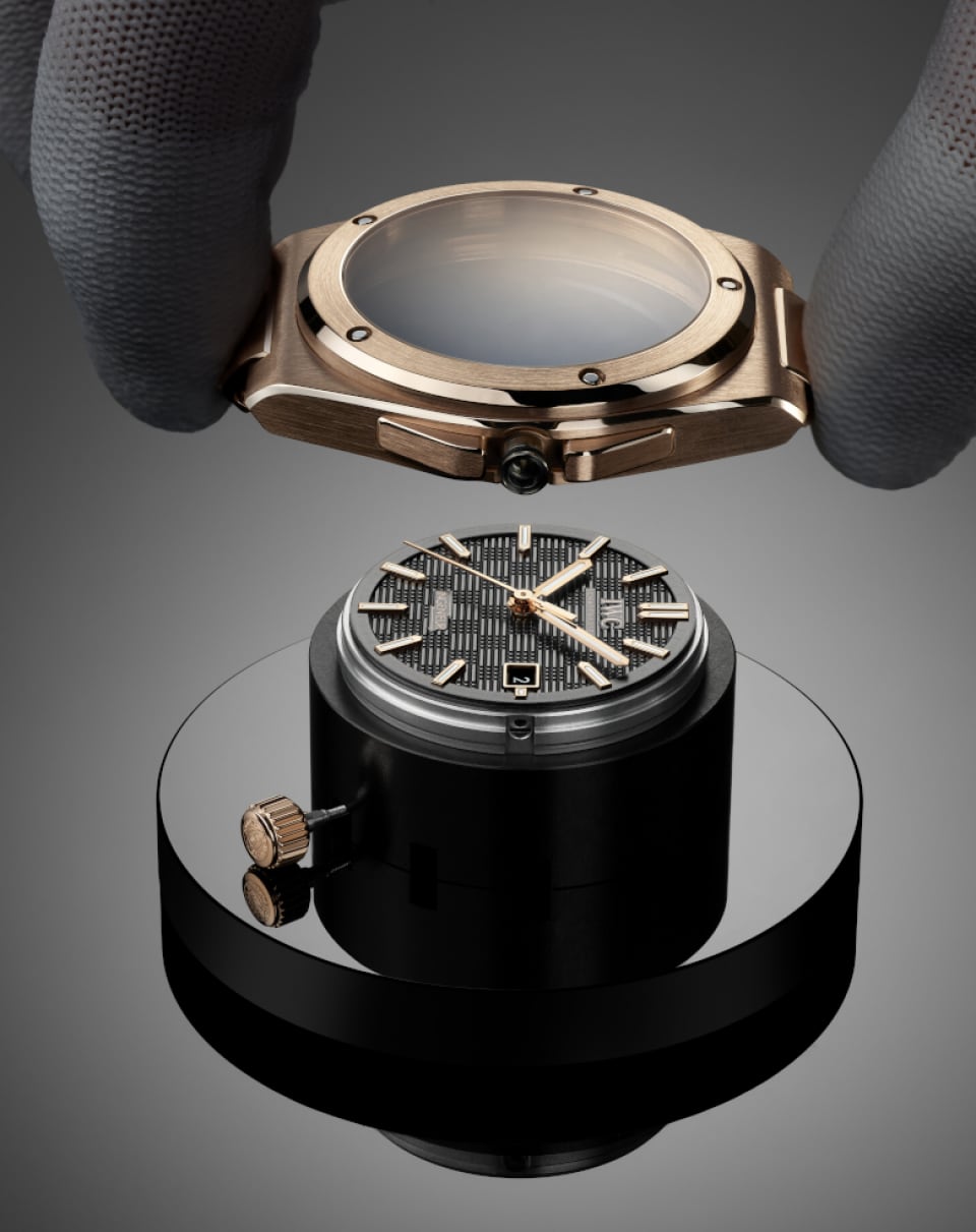 Hand with white gloves placing a gold case on the watch mechanism of IWC IW328702 Ingenieur Automatic 40.