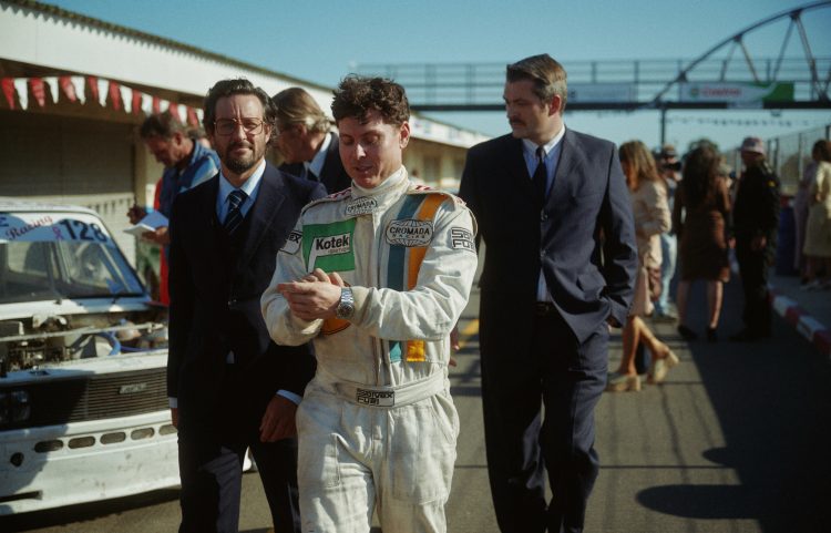 Racing driver with uniform wearing the IWC Ingenieur SL with two men in suits in background